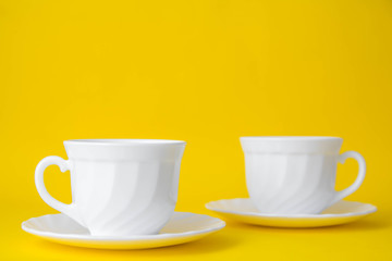 White ceramic cups with saucers on yellow background. White tableware crockery set. Space for text