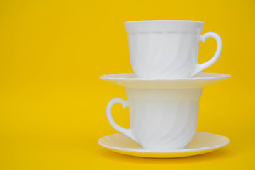 White ceramic cups with saucers on yellow background. White tableware crockery set. Space for text