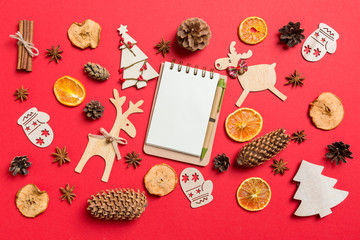 Top view of notebook, red background decorated with festive toys and Christmas symbols reindeers and New Year trees. Holiday concept