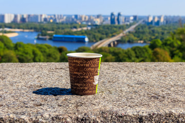 Paper cup of coffee on a stone parapet overlooking Kiev cityscape, Ukraine