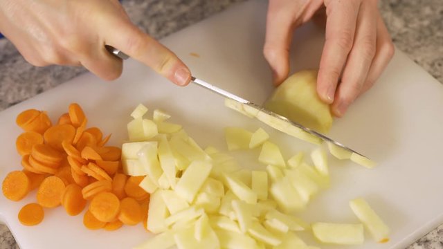 Woman cutting / chopping potatoes on white cutting board in home kitchen preparing meal by cutting vegetables
