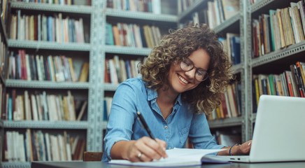 Young female student at the library. Young student reading book at library. Student learning for...