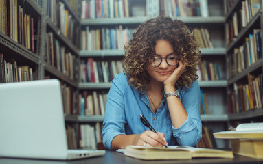 Young female student at the library. Young student reading book at library. Student learning for exam at library.
