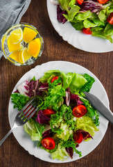 various fresh mix salad leaves with tomato in white plate on wooden background.