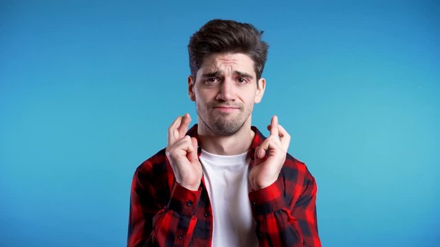  Handsome man in red shirt praying over blue background. European race guy begging someone. 4k. Religion concept.