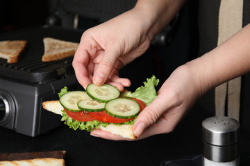 Woman adding cucumber to sandwich at black table, closeup