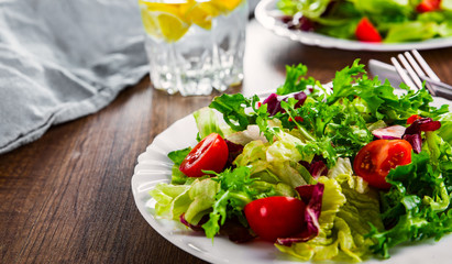 various fresh mix salad leaves with tomato in white plate on wooden background.