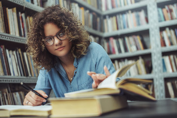 Young female student at the library. Young student reading book at library. Student learning for exam at library.