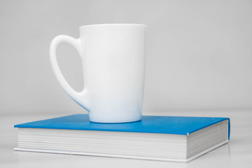 White ceramic cup and book on white table. Space for text