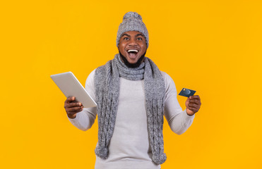 Excited afro guy holding digital tablet and credit card