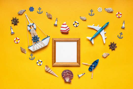 Heart symbol made of decorative items, miniature toys: seashells, vessel, anchors, lighthouses, life buoys. Sailboat and plane, empty wooden photoframe, mock up. Summer vacation, sea travel concept