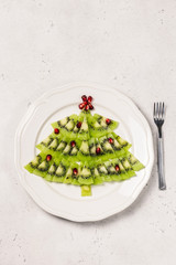 Holiday menu, kiwi pomegranete christmas tree on white plate. Top view, space for text.