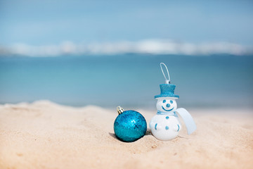 Naklejka na ściany i meble New Year's snowman in white in a blue hat on a background of a beautiful sea. Christmas and New Year holidays in the concept of warm countries.