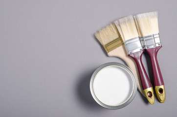 Open can with white paint and brush on gray background, top view. Space for text
