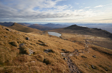 Looking down the trail from the summit of Slioch with a small Lochan to the left on a sunny winters day in the Scottish Highlands.