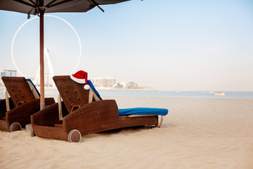 Sun loungers with santa hats on the beach with sea view. Christmas and New Year holidays in the concept of warm countries.
