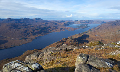 Views of Loch Maree and Flowerdale Forest in the distance from the rocky summit of Slioch in the Scottish Highlands on a sunny winters day.