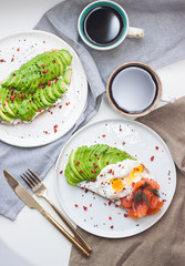 Toast with cream fresh, smoked salmon, poached egg and sliced avocado, and two cups of coffee. 
