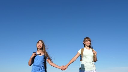girls, women travelers go holding hands on a background of blue sky. close-up. teamwork tourists teenagers. Women travelers walk across field. hiker girls in the summer on the meadow.