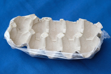 Empty egg tray close up. Cardboard egg tray in cellophane on a blue background. Disposable used paper egg container.