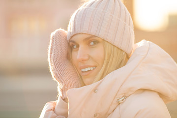 Obraz premium Portrait of a beautiful young model in pink knitted hat and mittens. Beautiful natural young smiling blonde woman wearing knitted gloves.
