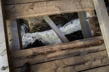 Looking down through a hole in a rotten wooden footbridge with the stream far below.
