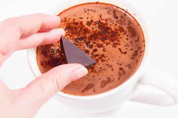 Cup of hot chocolate with a hand putting a piece of chocolate into it
