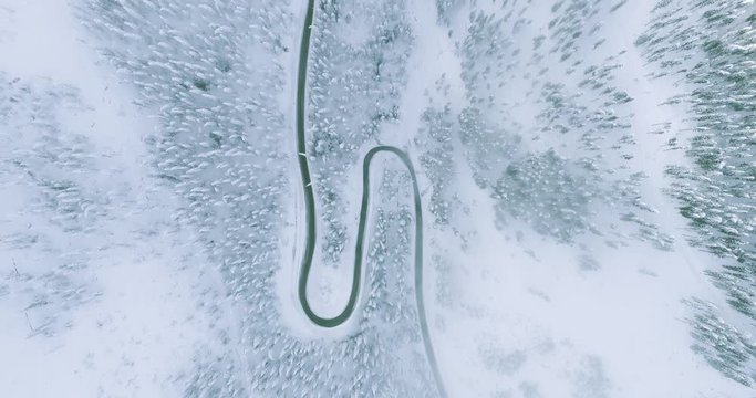 Beautiful aerial view of snow covered mountain landscape in winter time with curvy road cutting through forest and sea of clouds