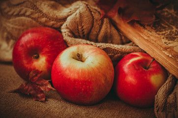 Close-up three red apples and old book with maple leaves on knitted blanket background