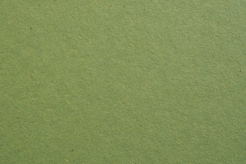 The surface of a sheet of green cardboard. Background or wallpaper. Rough paper texture with cellulose fibers. View from above. Macro