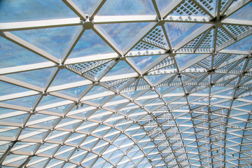 Abstract high-tech architecture background photo, internal structure of glass roof arch with lockable windows sections. Transparent glass roof of a modern building with blue sky and clouds