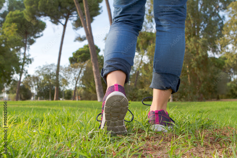 Wall mural Woman with sneakers and jeans walking on grass.