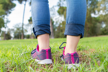 Woman with sneakers and jeans walking on grass. close up