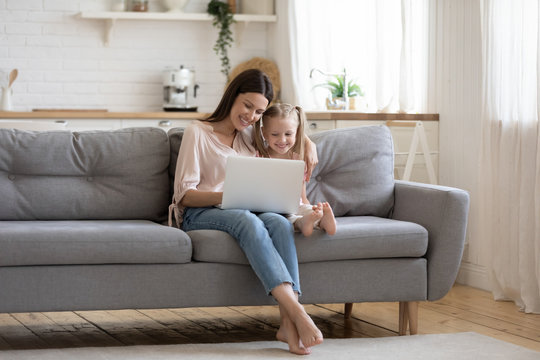 Loving mom teaching child daughter using laptop sit on sofa