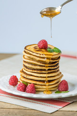 Pancakes with honey and raspberries on a white plate on a wooden table