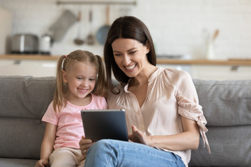 Cheerful mom with kid daughter using digital tablet at home