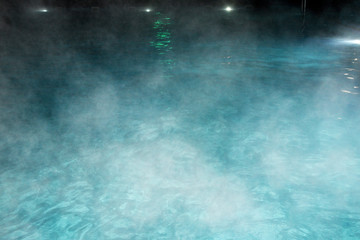 Pure clear water in the thermal pool. Hot water flows, and fog rises above the pool, the pool itself is illuminated by lanterns. Blue water, beautiful background. - obrazy, fototapety, plakaty