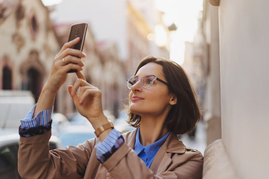 Portrait of woman taking pictures of beautiful view on smartphone while walking on the old european streets