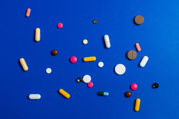 Close-up of assorted multi-colored pills on a blue background. Medical flat lay.