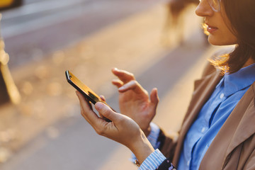 Thoughtful woman in eyeglasses wearing blue shirt ordering taxi via cab application on smartphone...