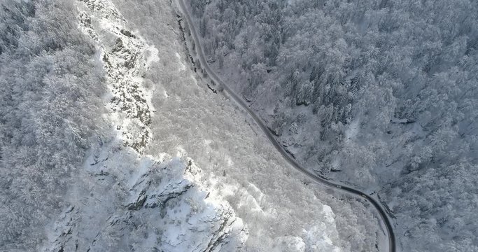 Aerial view of mountain road in winter time. Sunlit cliffs and snow covered forest
