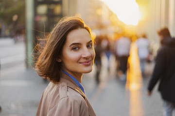 Portrait of positive cheerful woman tourist dressed in casual outfit looking at the camera on urban setting during sunny day