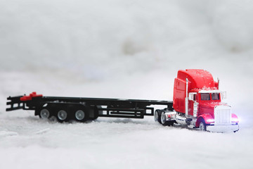 Toy tractor and red truck. Stands with the cargo container removed. Truck on a background of snowdrifts.