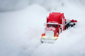 Toy red truck brings New Year and Christmas gifts. Winter holidays are coming. He rides through real snowdrifts. Winter shooting on the street. Headlights is on