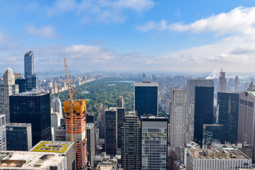Aerial view of New York with skyscrapers, buildings in construction and central park in the background. Sunny day with some clouds. Concept of travel and construction. NYC, USA
