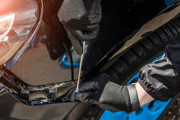 A man is trying to fix a car bumper. Screws in a screwdriver for fastening. Close-up of a hand in a...