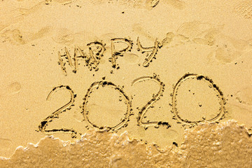 Inscription happy new 2020 on beach sand, wave covering text. New Year 2020 is coming concept.