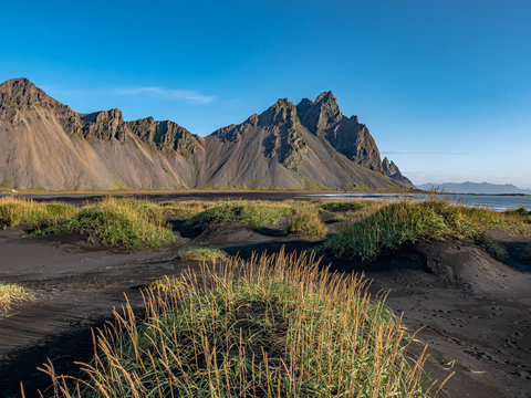 Epic aerial drone view flying over landscape of the black sand beach in Stokksnes on a sunny day. Vestrahorn mountain in the background. Nature and ecology concept background.