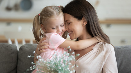 Happy mom embracing kid daughter holding spring flowers bouquet