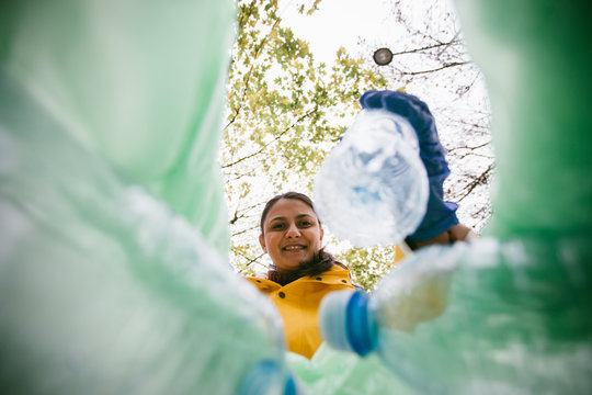 Volunteer with garbage bags collecting plastic bottles. Low angle view of girl cleaning park